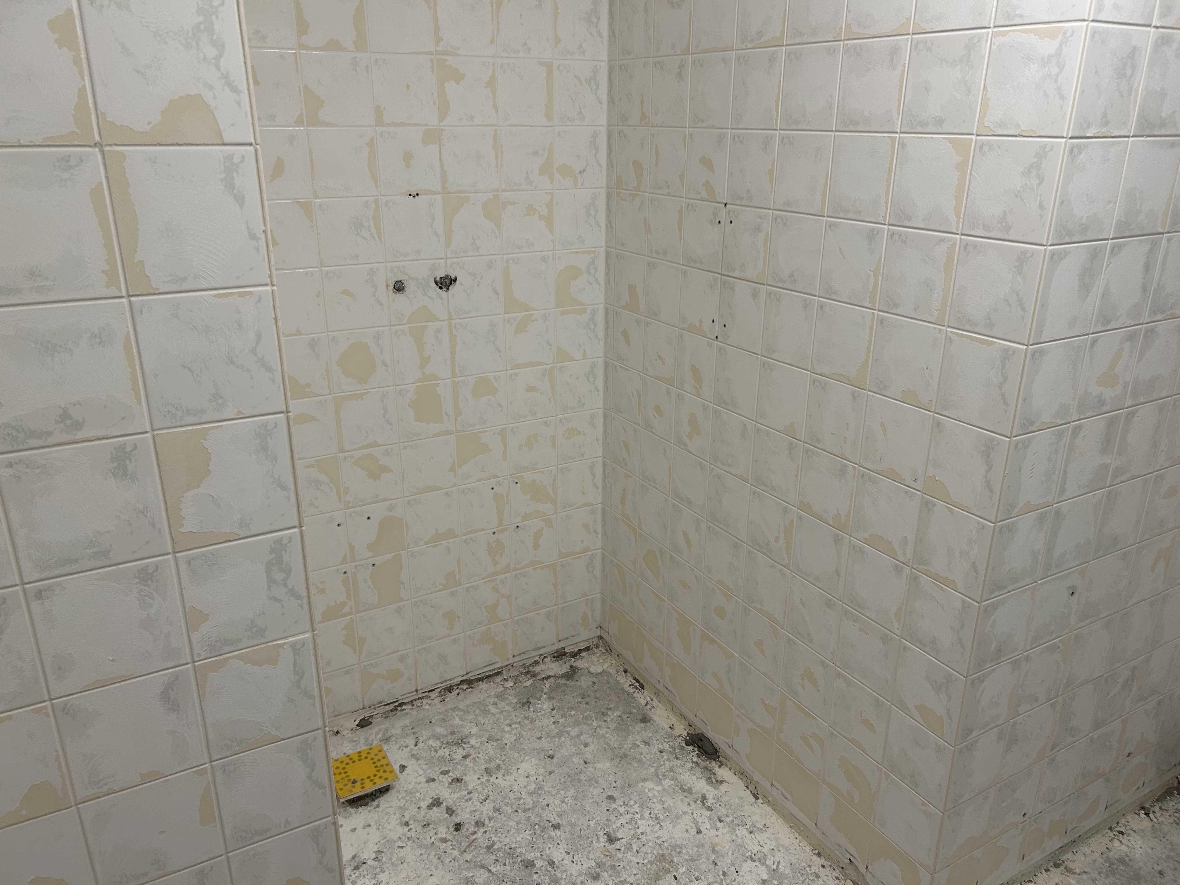 Detail van opgeruwde wandtegels en verwijderde vloer in badkamer.