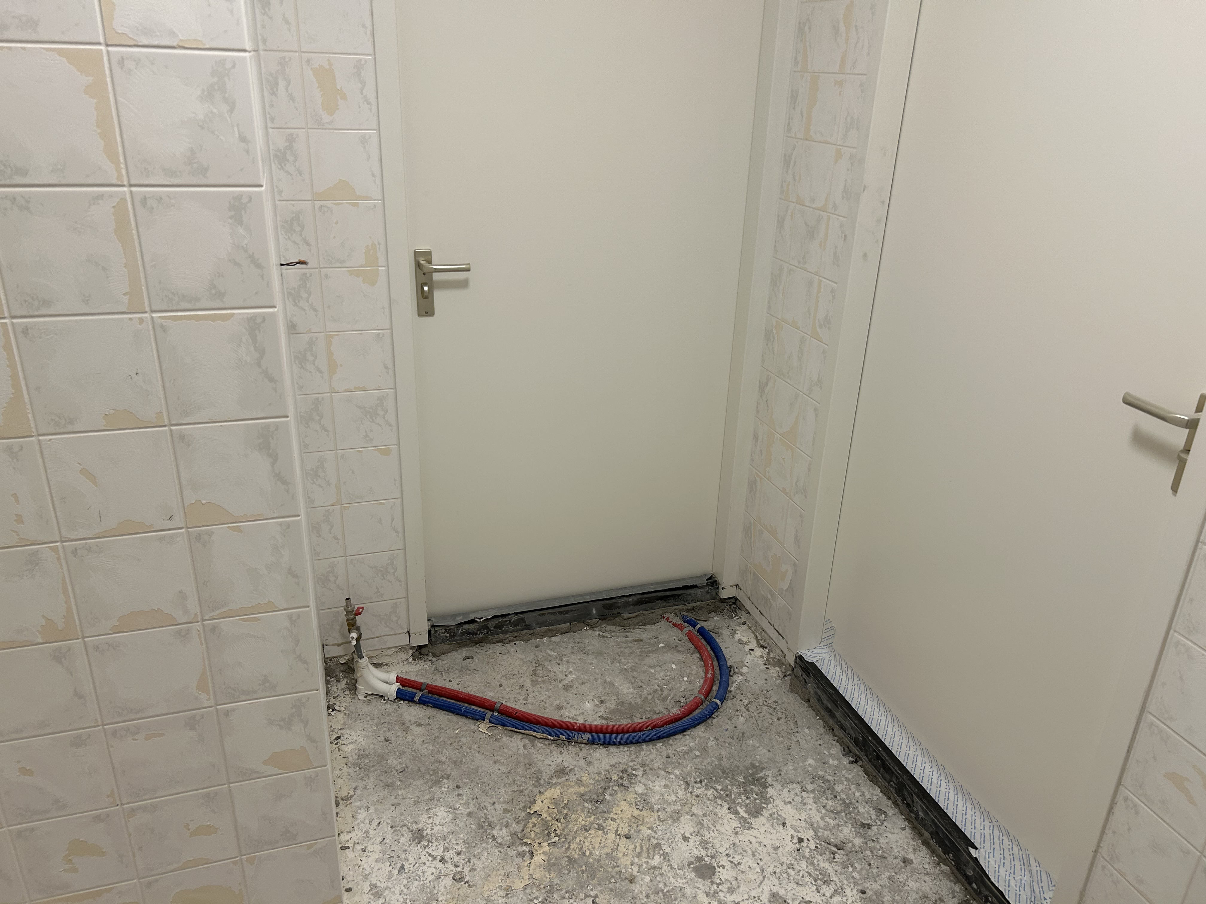 Overzicht van badkamer na sloopwerk, leidingen en ondervloer zichtbaar.