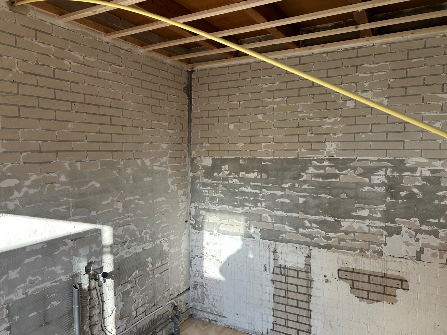 Keuken na sloop, muur tot op baksteen en lijmresten zichtbaar.